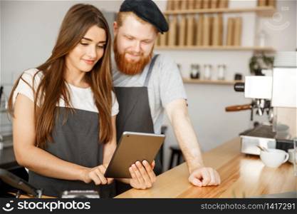 Coffee Business Concept - Satisfied and smile owners couple look on tablet orders online in modern coffee shop
