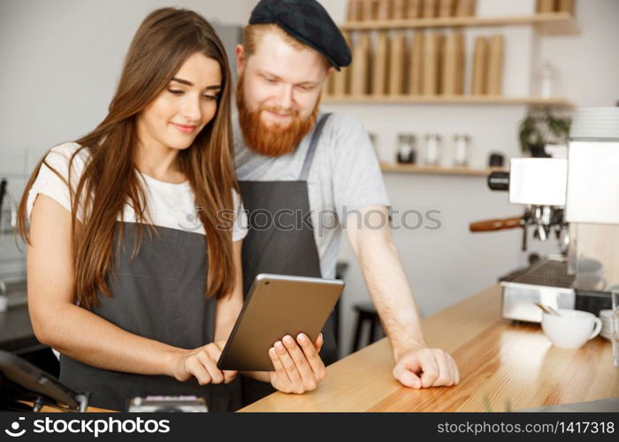 Coffee Business Concept - Satisfied and smile owners couple look on tablet orders online in modern coffee shop