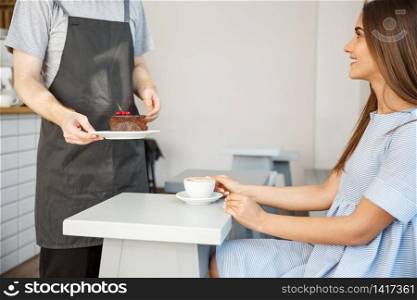 Coffee Business Concept - Waiter or bartender giving chocolate cake and talking with caucasian beautiful lady in blue dress at Coffee shop.