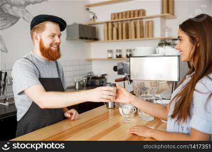 Coffee Business Concept - young beared handsome barista talking and giving take away hot coffee for beautiful caucasian customer in modern coffee shop.
