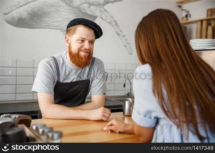 Coffee Business Concept - young beared handsome barista talking with beautiful caucasian customer in modern coffee shop.