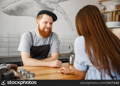 Coffee Business Concept - young beared handsome barista talking with beautiful caucasian customer in modern coffee shop.