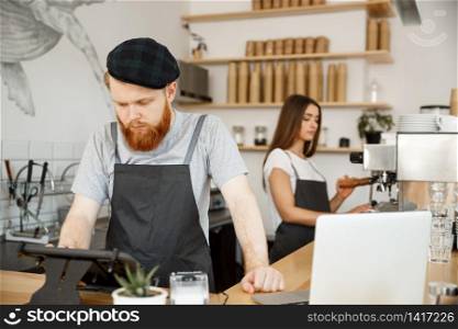 Coffee Business Concept - Young handsome bearded bartende, barista or manager posting the order from guest in digital tablet menu at modern coffee shop.