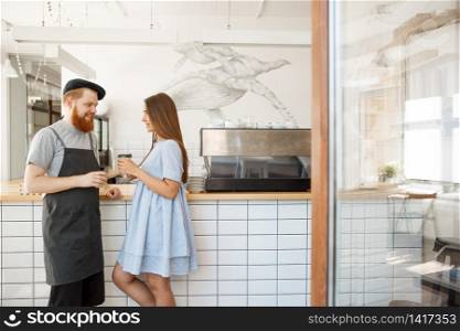 Coffee Business Concept - young smart bearded bartender enjoy talking and giving take away cup of coffee to pretty customer.