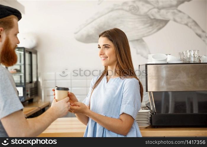 Coffee Business Concept - young smart bearded bartender enjoy talking and giving take away cup of coffee to pretty customer.