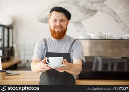 Coffee Business owner Concept - Portrait of happy young bearded caucasian barista in apron with confident looking servicing hot coffee to customer in coffee shop counter.