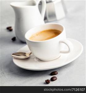 Coffee composition on white concrete background. Coffee espresso in white cup with milk and coffee maker. Breakfast concept