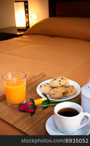 Coffee, cookies, orange juice and a pair of roses over the bed for a romantic breakfast in an orange predominant image.