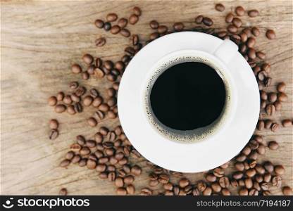 Coffee cup and coffee beans on table / black coffee in white mug on wooden background , top view