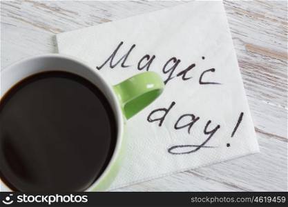 Coffee cup and napkin with message. Magic day message written on napkin on wooden table