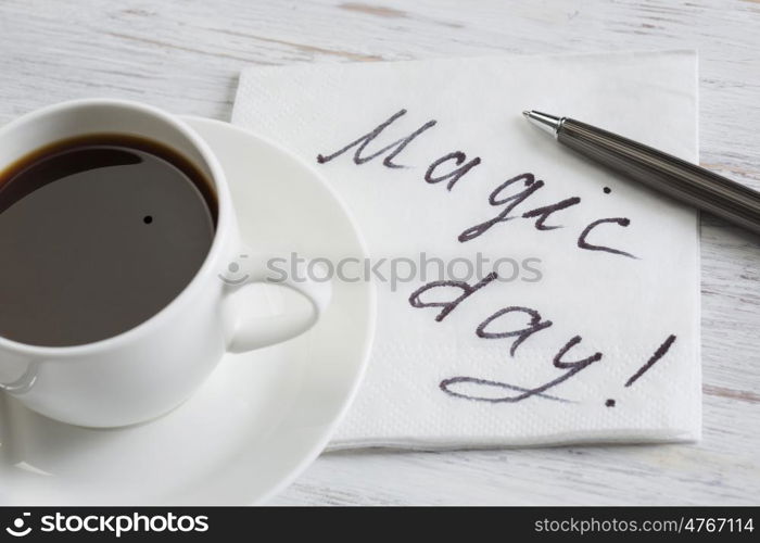 Coffee cup and napkin with message. Magic day message written on napkin on wooden table