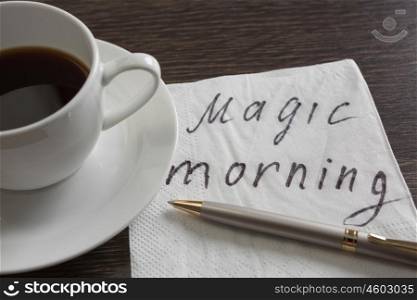 Coffee cup and napkin with message. Magic morning message written on napkin on wooden table