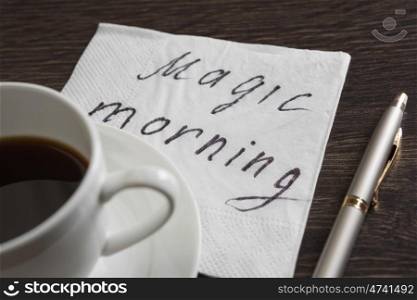Coffee cup and napkin with message. Magic morning message written on napkin on wooden table