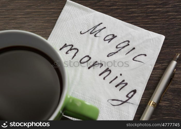 Coffee cup and napkin with message. Magic morning message written on napkin on wooden table