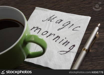 Coffee cup and napkin with message. Magic morning message written on napkin on wooden table