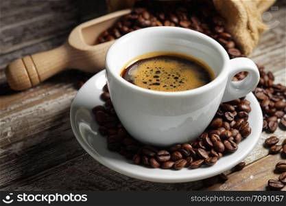 Coffee cup and roasted coffee beans in a burlap sack on a wooden rustic table close up view on rusty vintage background.