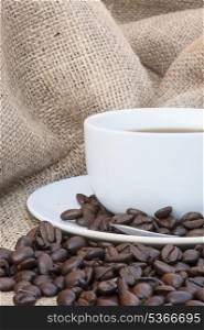 Coffee cup and saucer on hessian cloth surrounded by coffee beans