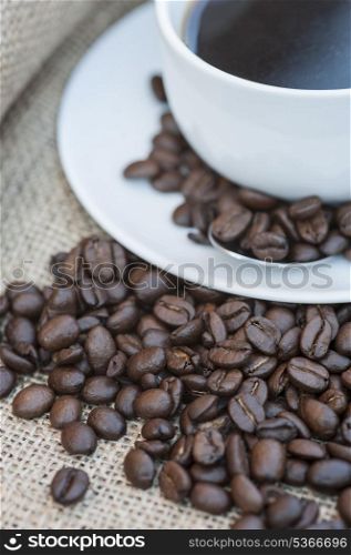 Coffee cup and saucer on hessian cloth surrounded by coffee beans