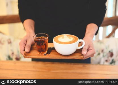 Coffee cup in hand on wooden table in cafe with coffee beans background, Served Coffee Cappuccino or latte and Tea