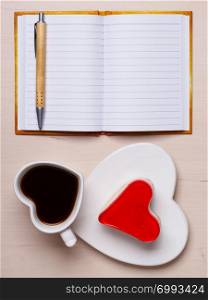Coffee cup jelly cake in form of heart and paper blank notebook with pen on desk, top view copy space for text