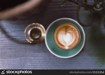 Coffee cup latte art with green saucer on wood background