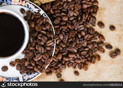 Coffee cup on roasted coffee beans on sack and rustic wood background top view