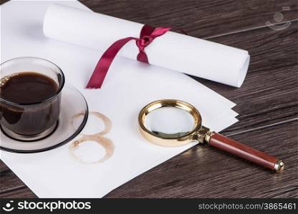 Coffee cup, paper sheets and detective magnifying glass on old Wooden table.