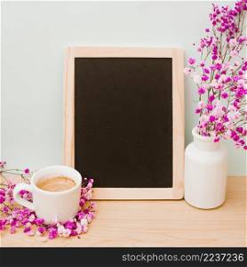 coffee cup pink baby s breath vase near blank wooden slate desk against wall