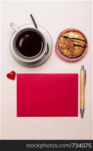 Coffee cup sweet cake cupcake and red paper blank with pen on wooden surface, top view copy space for text