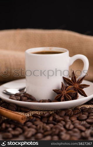 Coffee cup with burlap sack of roasted beans on rustic table