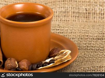 Coffee cup with cinnamon, coffe beans, nuts and lemon over sacking