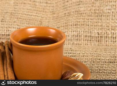 Coffee cup with cinnamon, coffe beans, nuts and lemon over sacking