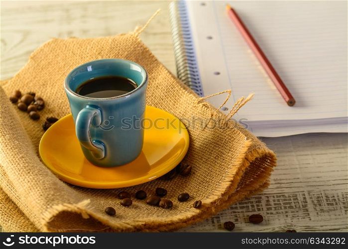 coffee cup with coffee beans liyng in the background with a book for taking notes on side