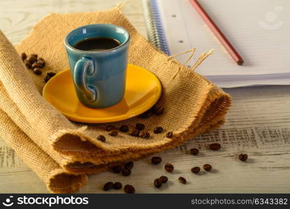 coffee cup with coffee beans liyng in the background with a book for taking notes on side