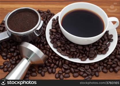 Coffee cup with portafilter and tamper on coffee bean background