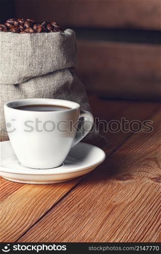 Coffee cup with saucer, beans and burlap bag on wooden background. Coffee cup with saucer, beans and burlap bag