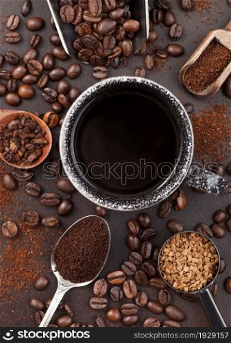 Coffee cup with various scoops of ground and bean coffee and freeze dried instant coffee granules on brown background. Top view
