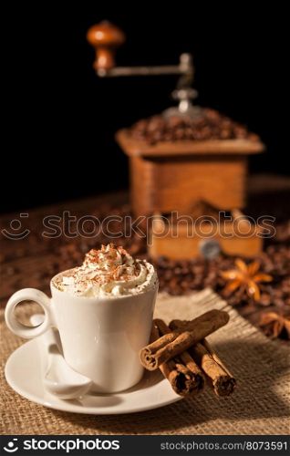 Coffee cup with whipped cream and cocoa powder and coffee grinder on background. Coffee cup with whipped cream and coffee grinder on background