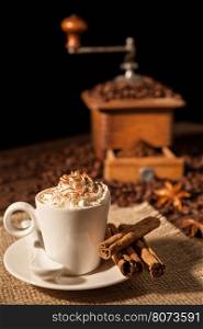Coffee cup with whipped cream and cocoa powder and coffee grinder on background. Coffee cup with whipped cream and coffee grinder on background