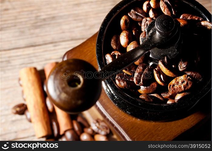 Coffee grinder with beans on the wooden background with cinnamon sticks