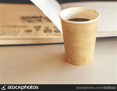Coffee in a recyclable paper disposable glass with an open notebook in background. Relaxing break and environmental safeguard