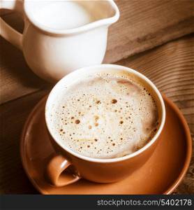 Coffee in brown cup and milk on wood background closeup