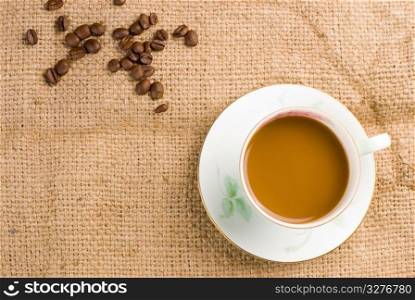 Coffee in white ceramic cup with coffee beans on burlap background