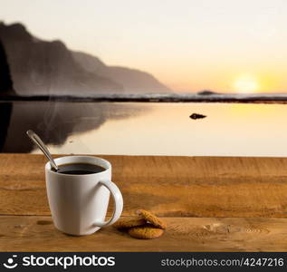 Coffee in white pottery cup on old wooden table with blurred image of kauai coast ocean at sunset or sunrise