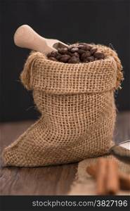 Coffee on burlap sack of roasted beans on rustic table.