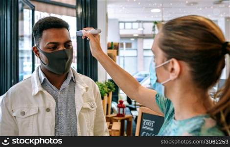 Coffee shop owner checking customers for fever upon entering. Business owner checking customers for fever