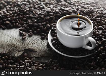 Coffee splash in white cup over roasted coffee beans background