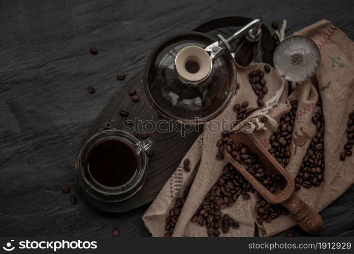 Coffee style, Cup of coffee and coffee beans roating with old wooden scoop and coffee beans around on the wooden and dark stone background. Top view with copy space for your text.