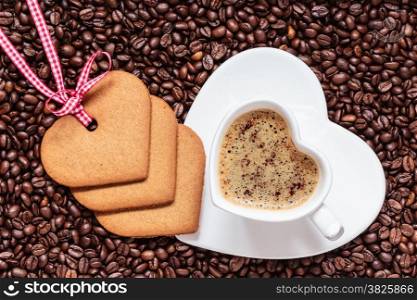 Coffee time concept. Heart shaped cup with cappuccino mocha and cookies gingerbread on coffee beans background. Top view