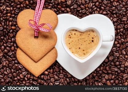 Coffee time concept. Heart shaped cup with cappuccino mocha and cookies gingerbread on coffee beans background. Top view